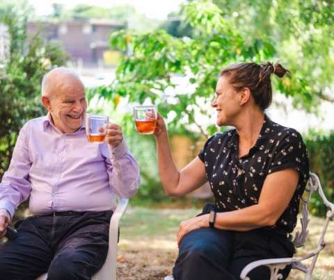 A younger and older person sitting in chairs sharing a drink.